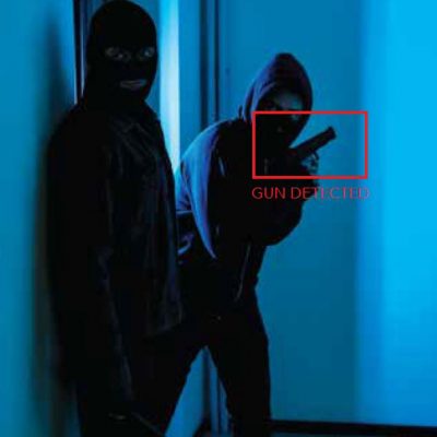 Two masked individuals in dark clothing inside a dimly lit hallway, with one holding a gun highlighted by a red detection box labeled "GUN DETECTED."