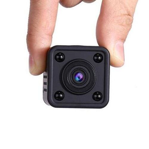 Person holding a small black hidden mini security camera between two fingers.